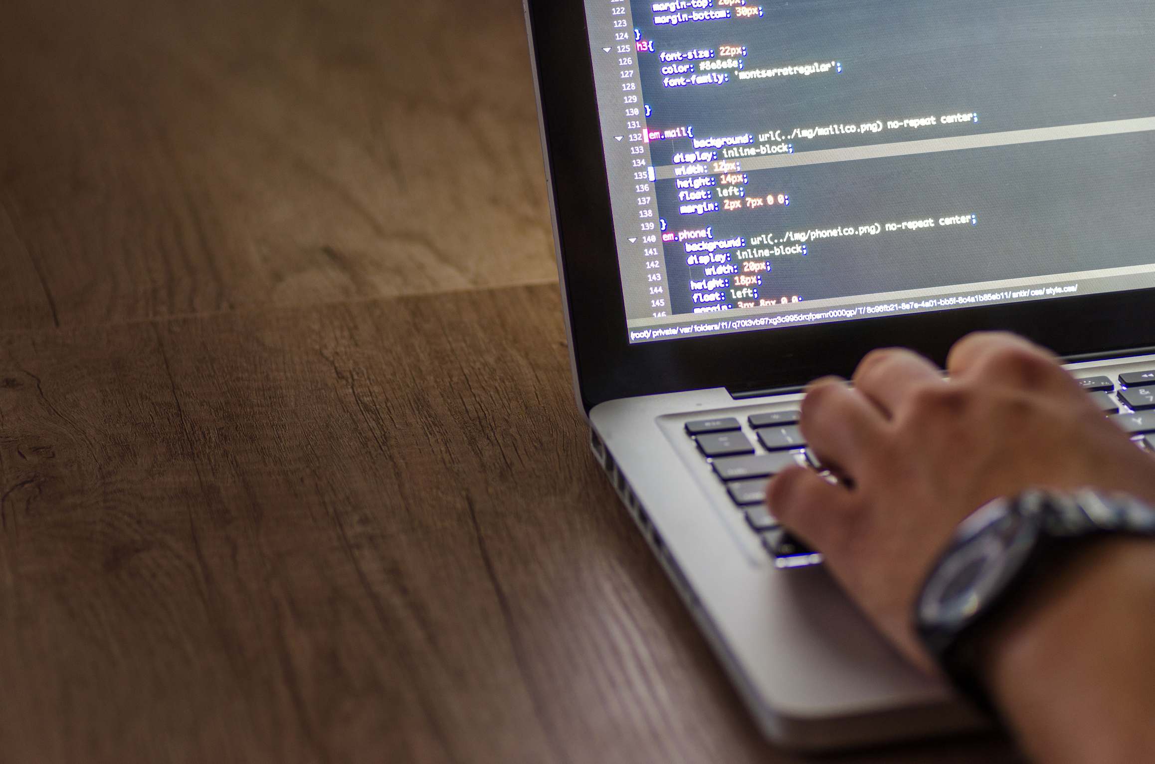 Close view of a keyboard and monitor showing code on a laptop screen with programming script